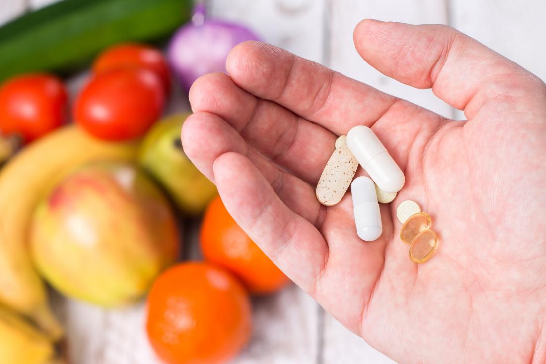 Person Holding Fat Soluble Vitamin Supplements Over Array Of Fruit And Vegetables.jpg