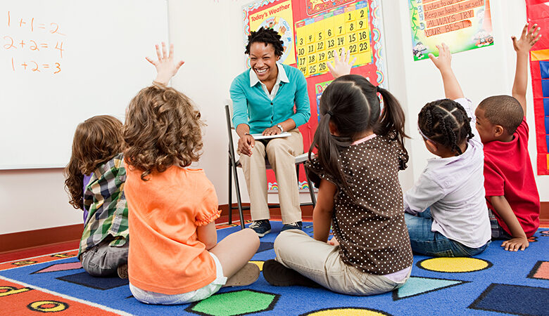 lærer og barn sitter på gulv med hendene hevet