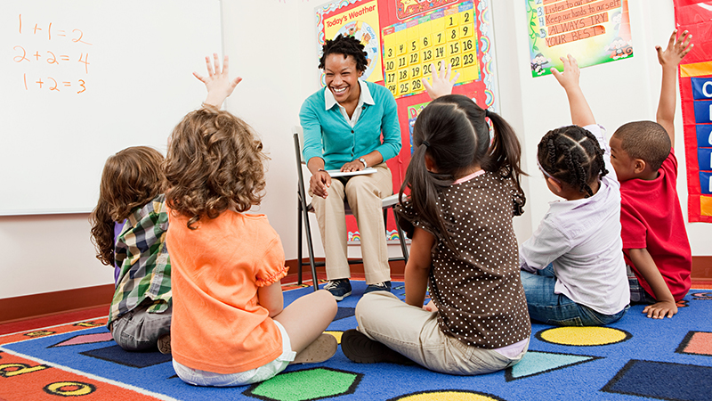 teacher and children sitting on floors with hands raised